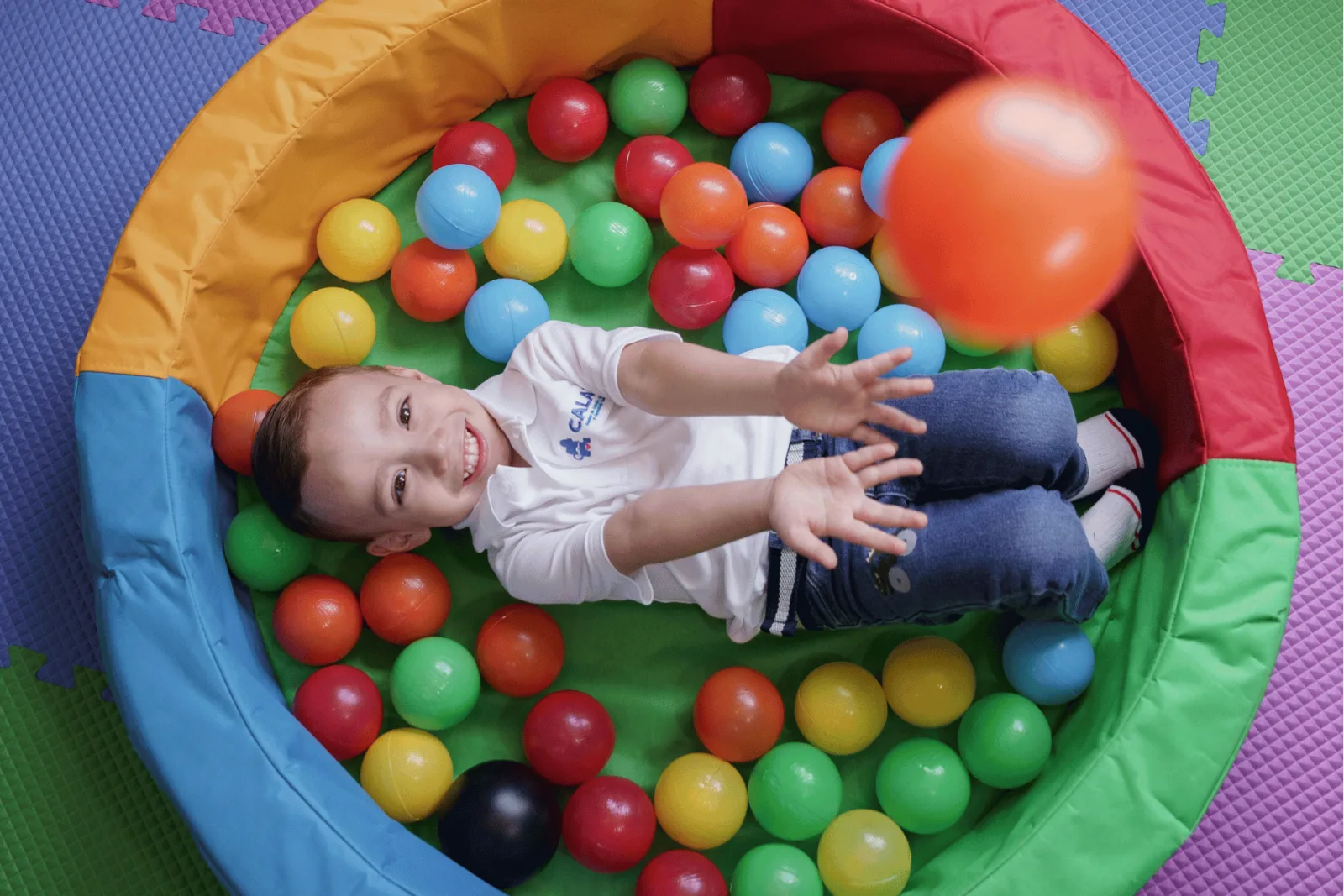 Una niña sonríe mientras juega con una pelota en una piscina de pelotas
